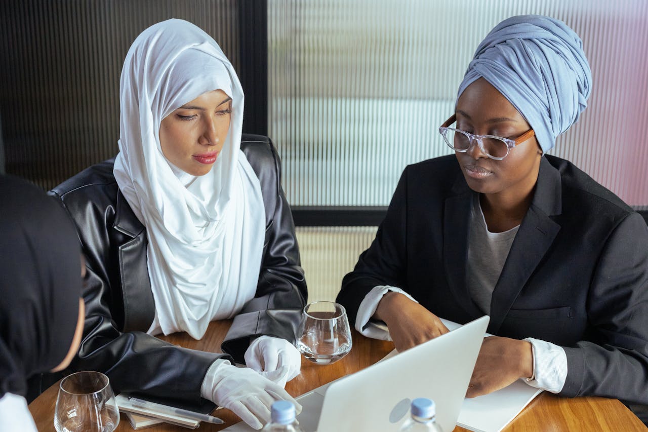 Two women in traditional attire collaborating on a laptop in a modern office setting.
